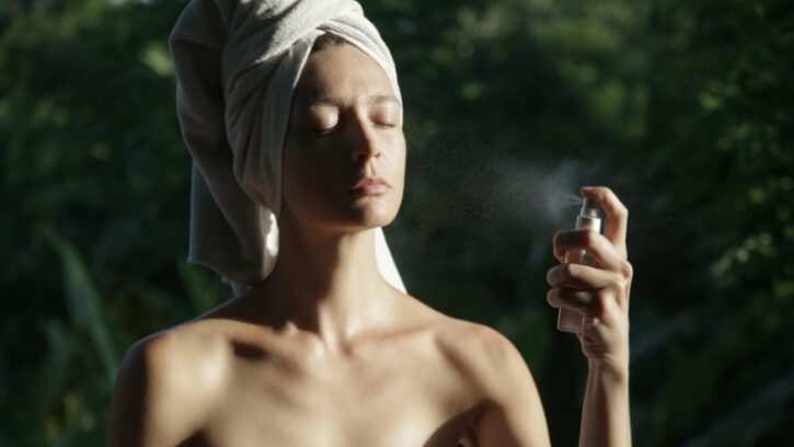 Žena sa peškirom na glavi prska lice hidrolatom na otvorenom