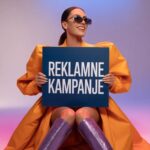 Zena u narandzastoj jakni drzi tablu sa natpisom Reklamne kampanje na kolor pozadini